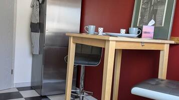 Eine kleine Küche mit einem Edelstahl-Kühlschrank, einem Holztisch mit zwei Barhocker und einem gerahmten Bild an der Wand.