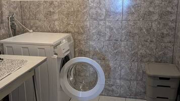 Une petite buanderie équipée d’un lave-linge, d’un sèche-linge et d’une poubelle.