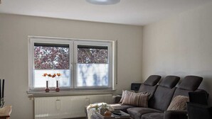 Un salon avec un sol à carreaux, un canapé, une table basse et une fenêtre avec des stores.