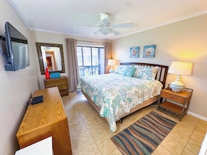 A hotel room with a bed, a desk, a television, a ceiling fan, and a window with curtains.