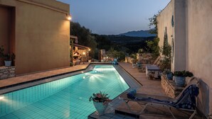 A swimming pool with a stone wall on one side and a lounge area with a table and chairs. - Kritiko Archontiko, Nature & Private Pool Escape

 (C6Q2+MP Aspro, Greece)
