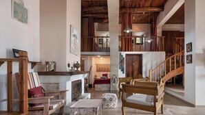 A spacious living area with wooden furniture, a fireplace, and a staircase leading to an upper level. - Kritiko Archontiko, Nature & Private Pool Escape

 (C6Q2+MP Aspro, Greece)