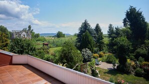 Un balcon donnant sur un jardin et sur des collines lointaines.