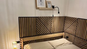 A bedroom with a wooden bed frame, a bedside table with a lamp, and a wall-mounted shelf with framed items. - SeaSide Apartment Salerno (Salerno)