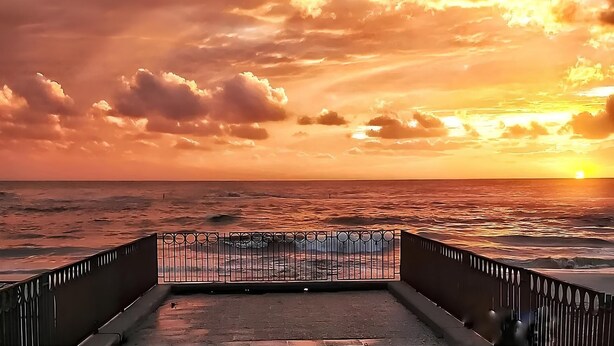 A sunset view from a pier with a metal railing, overlooking the ocean. - SeaSide Apartment Salerno (Salerno)