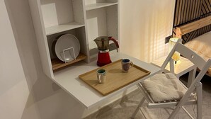 A modern kitchen with white cabinetry, a red kettle, and a wooden tray on the counter. There are two white cushioned chairs and a small table with a cup and saucer. - SeaSide Apartment Salerno (Salerno)