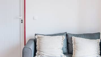 A room with a grey sofa, two striped pillows, a white door with a red frame, and a wall-mounted air conditioner.