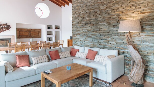 A modern living room with a sectional sofa, wooden coffee table, and a stone wall.