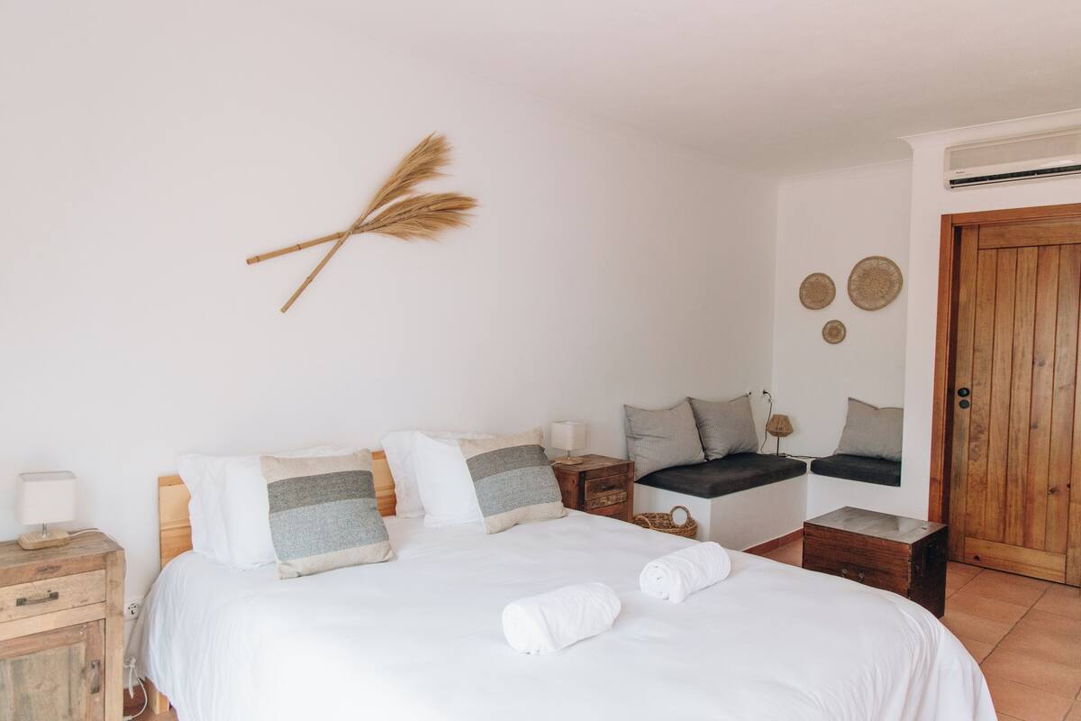 A bedroom with a bed, bedside tables, a window seat, and a wooden door.