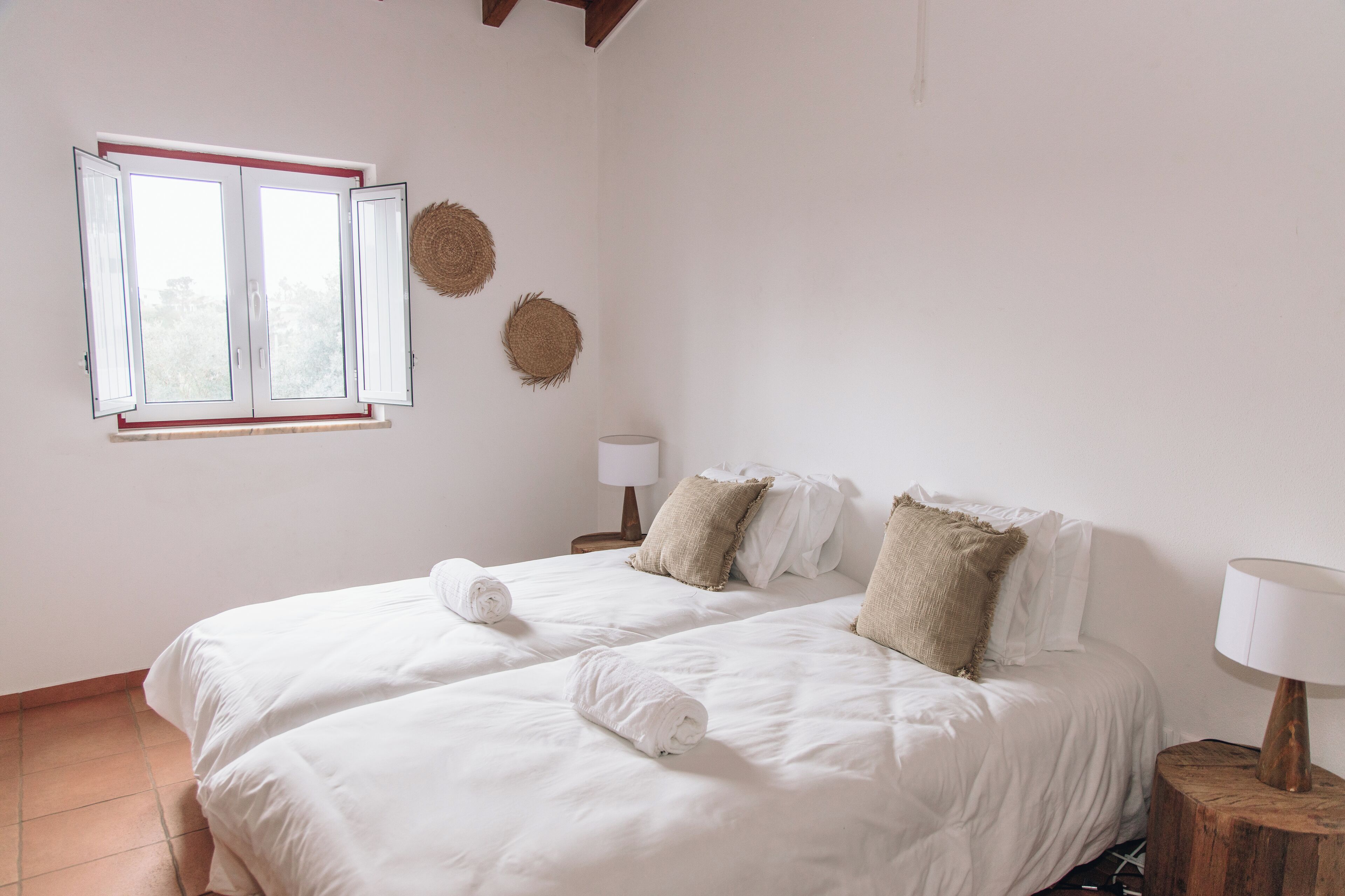 A hotel room with a large bed, two bedside tables, a window with blinds, and a wall-mounted lamp.