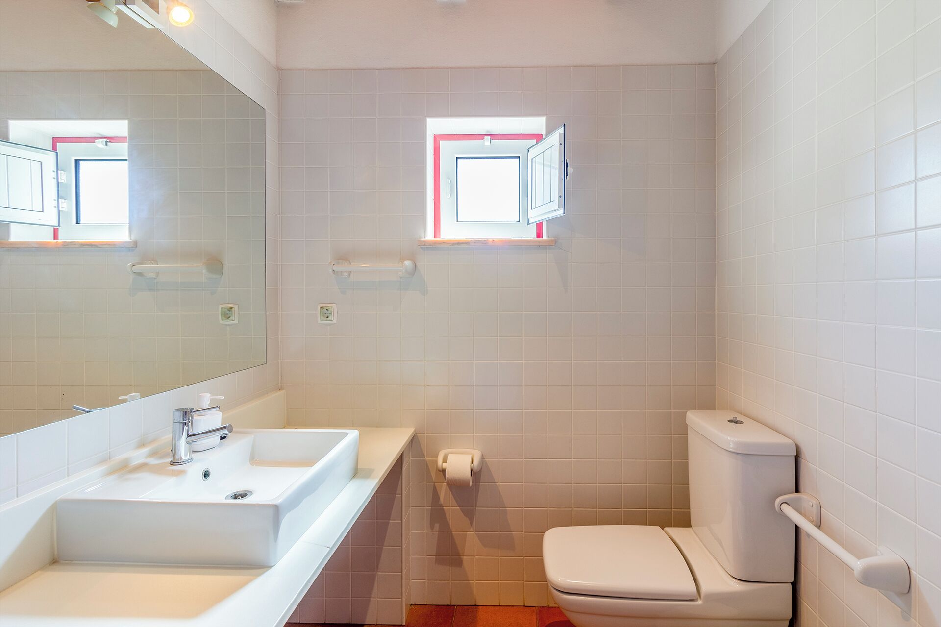Un baño moderno con lavamanos, espejo y retrete blancos.