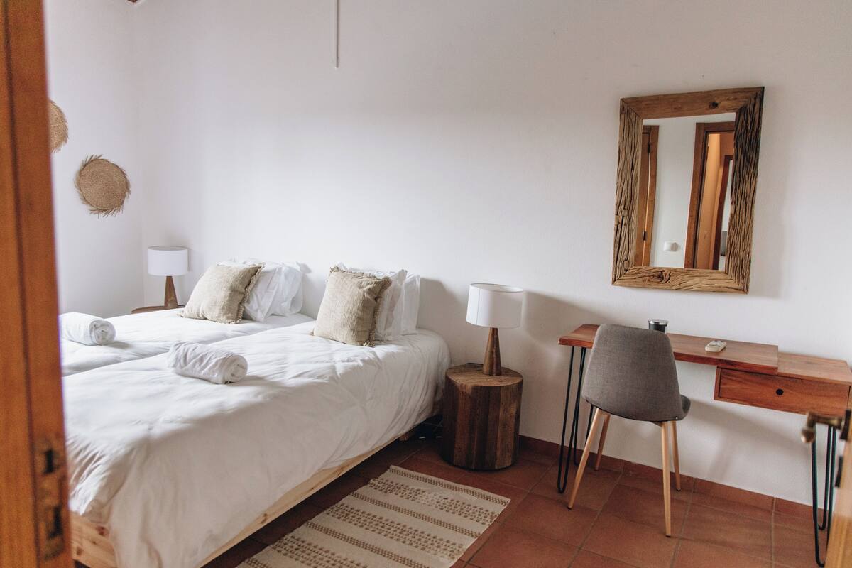 A bedroom with a bed, bedside table, lamp, chair, desk, and a mirror.