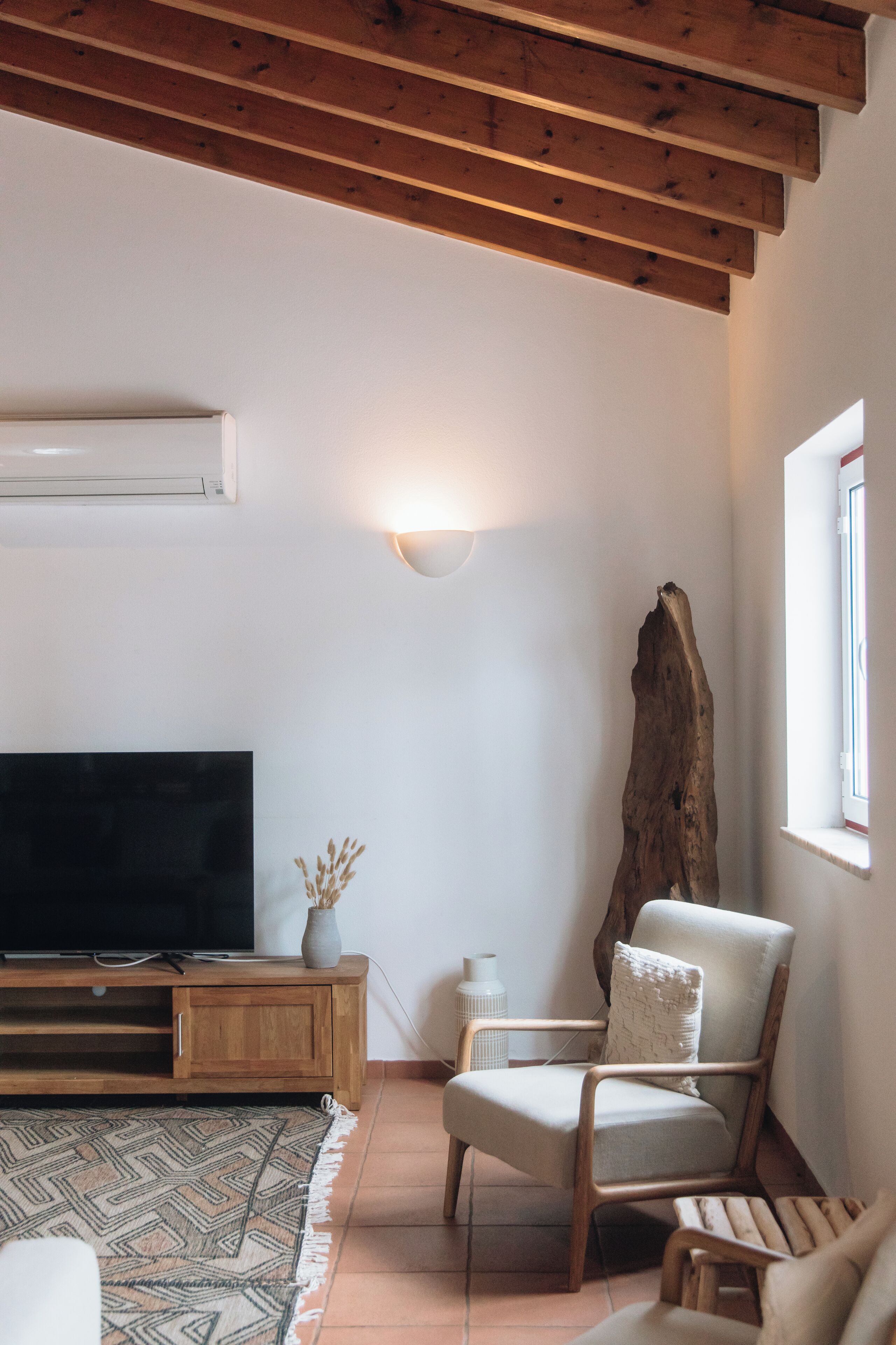 Una sala de estar con techo de madera, un televisor sobre un mueble de madera, una silla y un trozo grande de madera a la deriva.