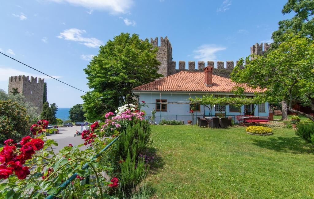 A building with a red-tiled roof, surrounded by lush greenery and a castle in the background.