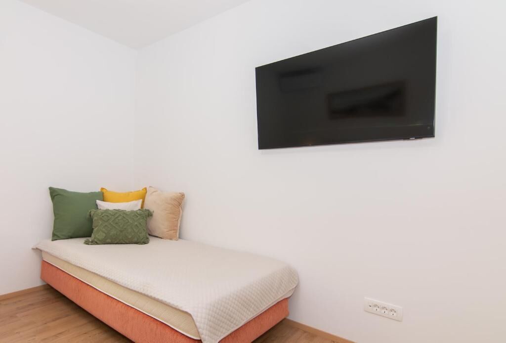 Ein Schlafzimmer mit einem Bett, Kissen, einem flachbildfernseher an der Wand und einer Steckdose.