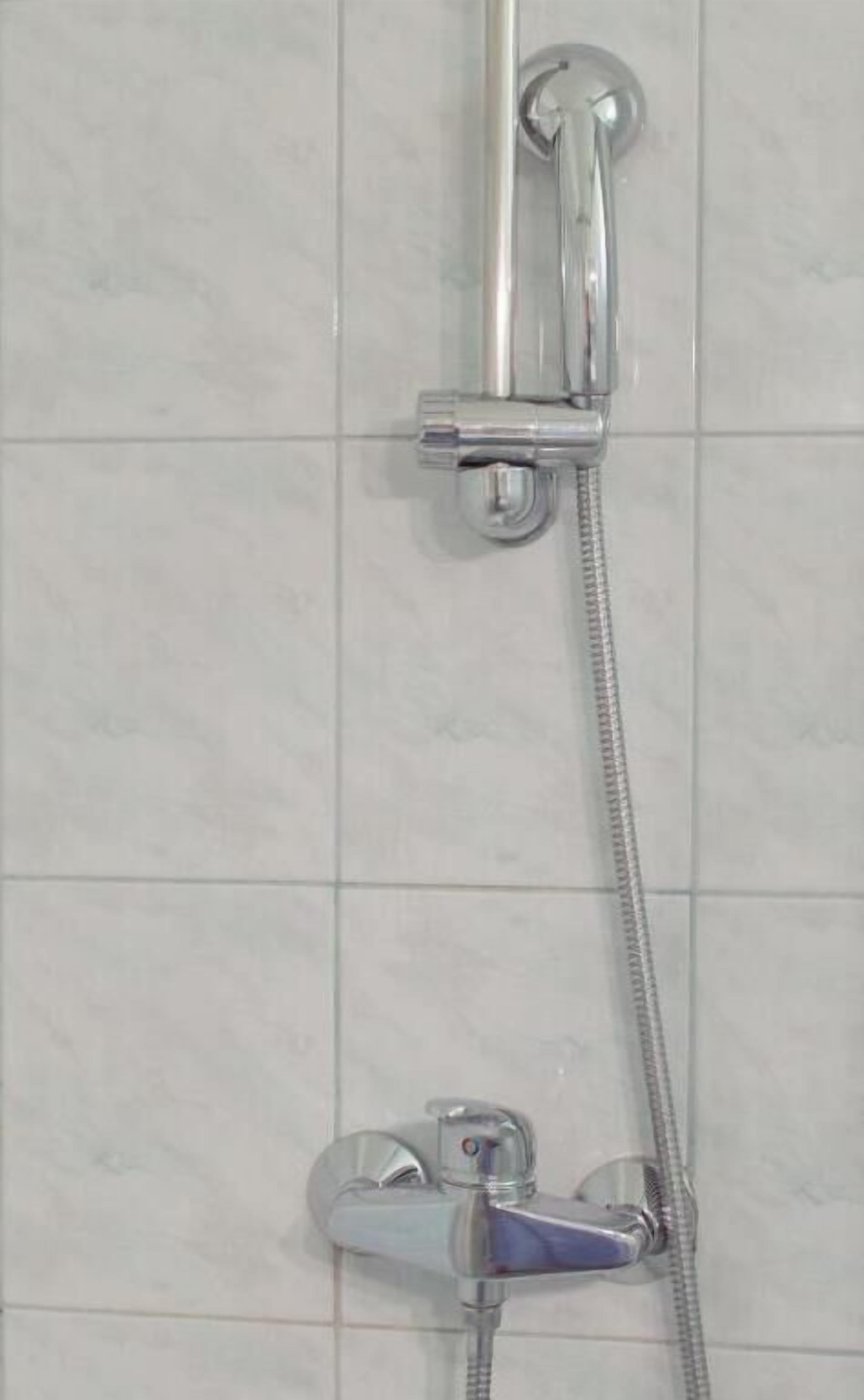 A shower with a handheld showerhead and a fixed showerhead, both mounted on a wall with tiled flooring.