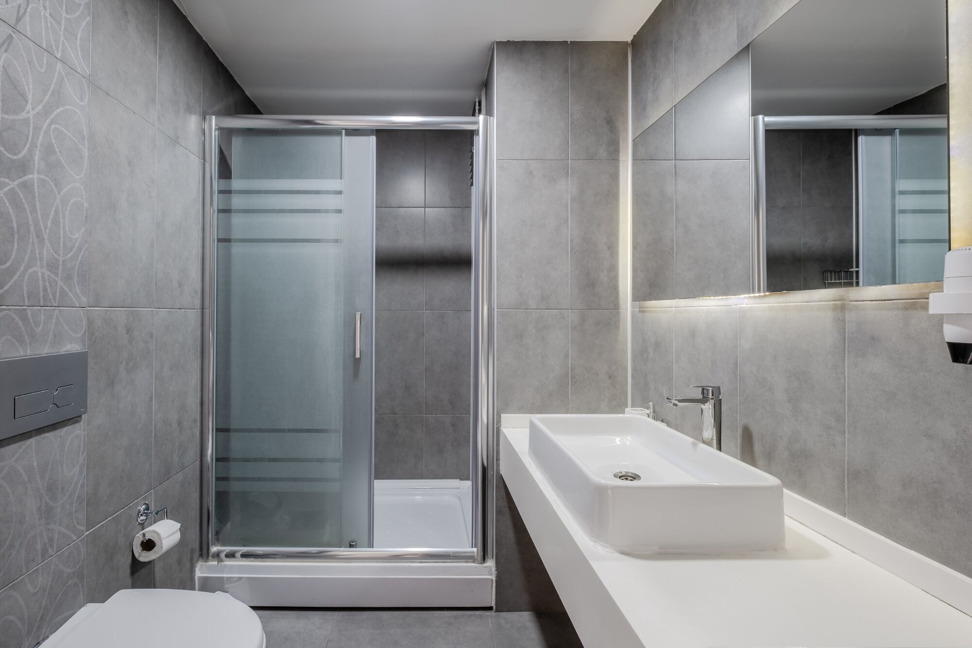 Uma casa de banho moderna com cabine de duche em vidro, lavatório branco e sanita.