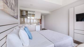 Une chambre d’hôtel de taille modeste, comprenant un lit, une petite kitchenette, un téléviseur et un tableau au mur.
