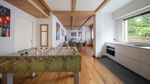 Een moderne keuken met houten balken, een tafelvoetbaltafel en een groot raam met uitzicht op groen.