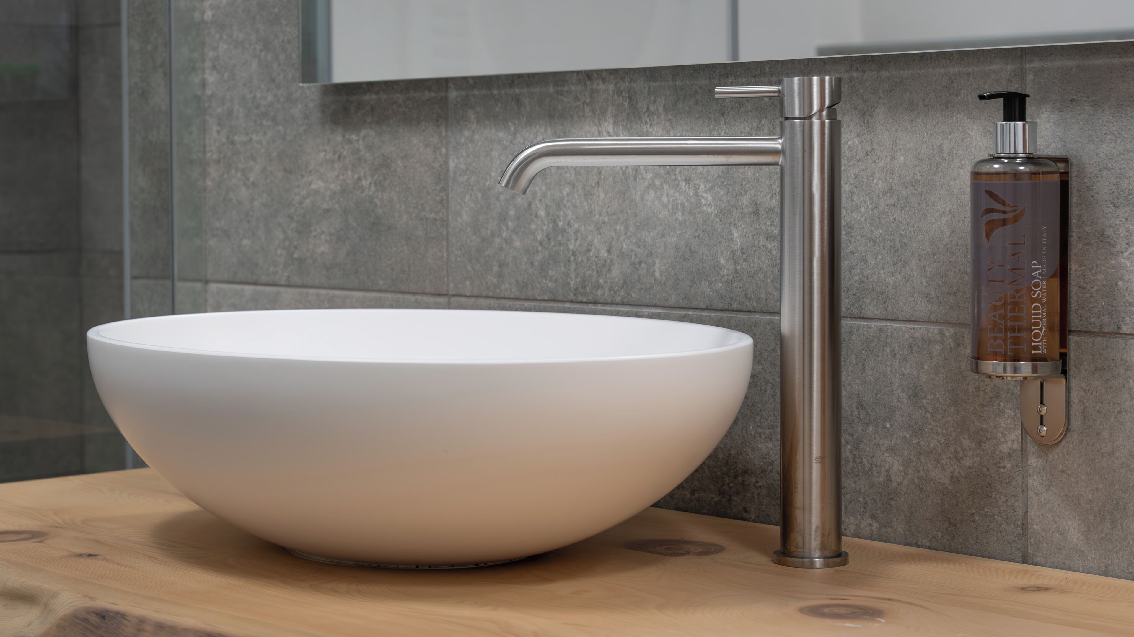 A modern bathroom with a large white vessel sink, a sleek faucet, and a bottle of Beauty Thermal liquid soap.