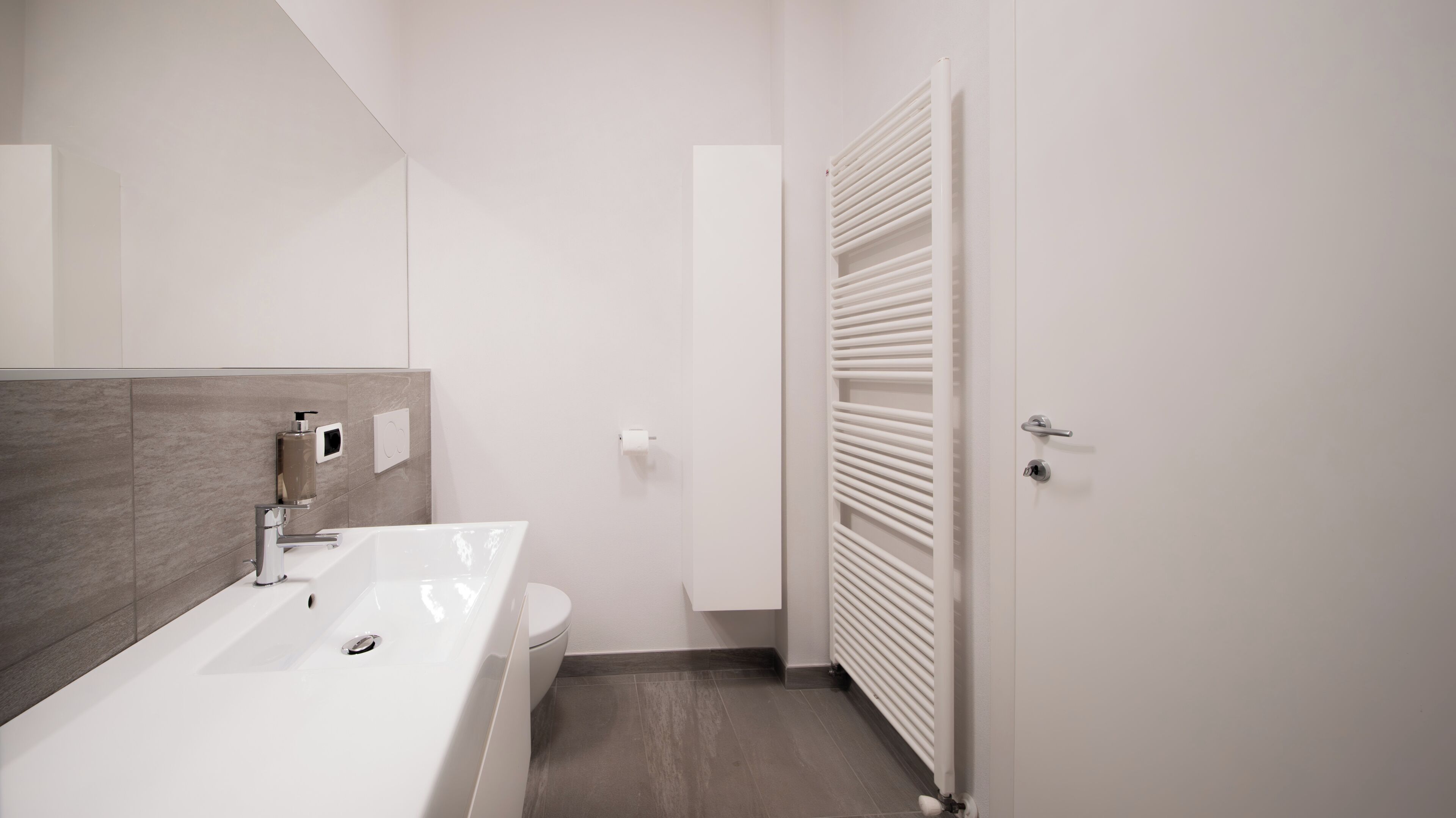 Een moderne badkamer met een witte wastafel, toilet en handdoekhouder.