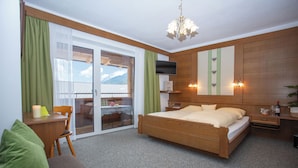 Ein Hotelzimmer mit einem hölzernen Bett, einem Schreibtisch mit Stuhl, einem Fernseher und Blick ins Freie.