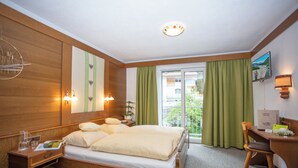 Ein Hotelzimmer mit einem hölzernen Bett, Nachttischen, einem Schreibtisch und Blick ins Freie durch eine Schiebetür.