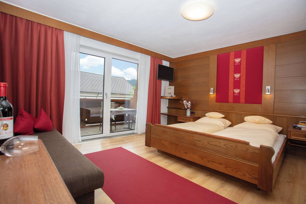 Ein Hotelzimmer mit einem hölzernen Bett, einer Couch, einem Fernseher und einem Balkon mit Bergblick.