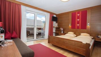 Una camera d'albergo con un letto in legno, una poltrona, una televisione e un balcone con vista sulle montagne.