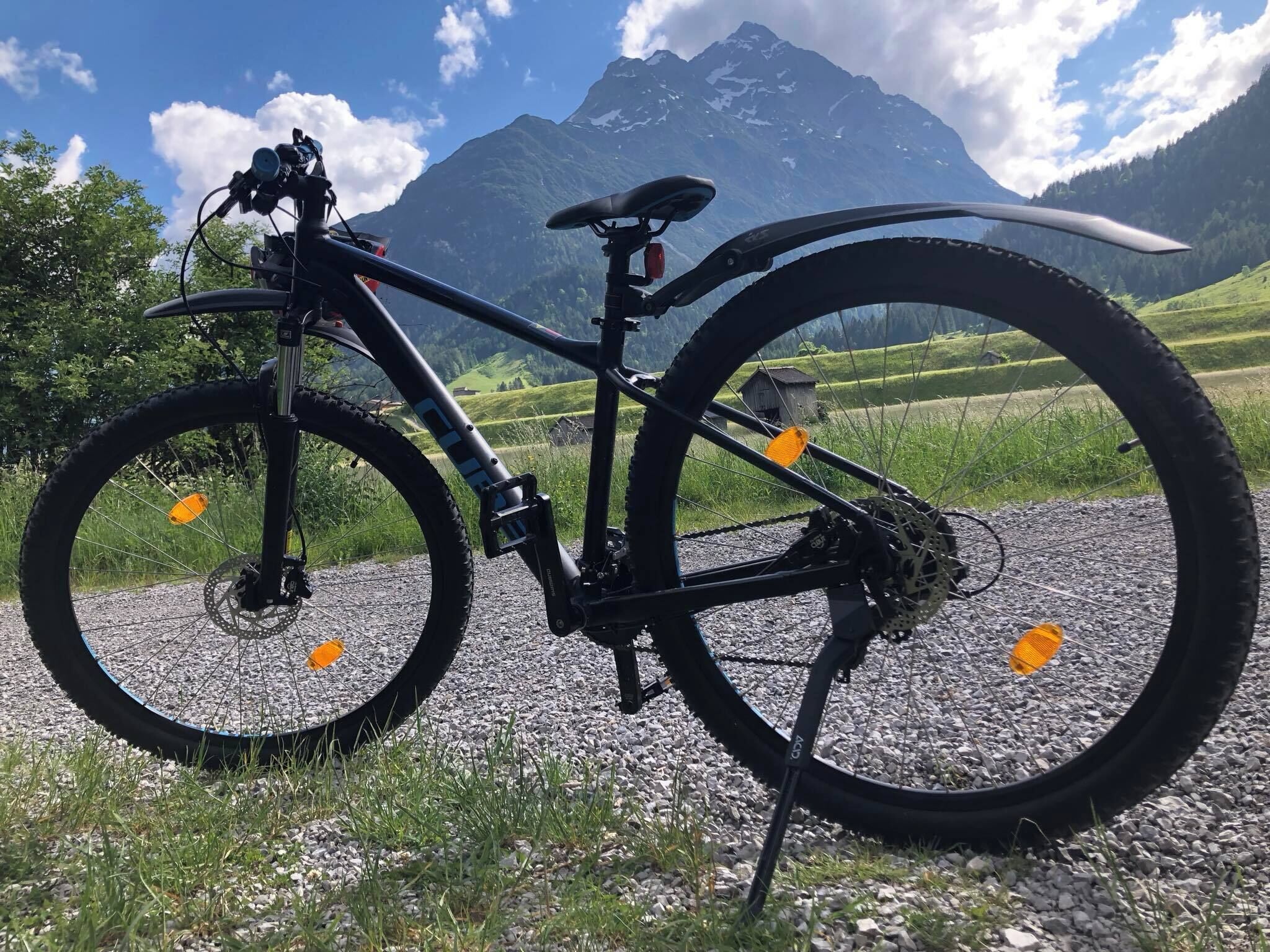 Una bicicleta de montaña estacionada en un camino de grava con una vista panorámica de la montaña al fondo.