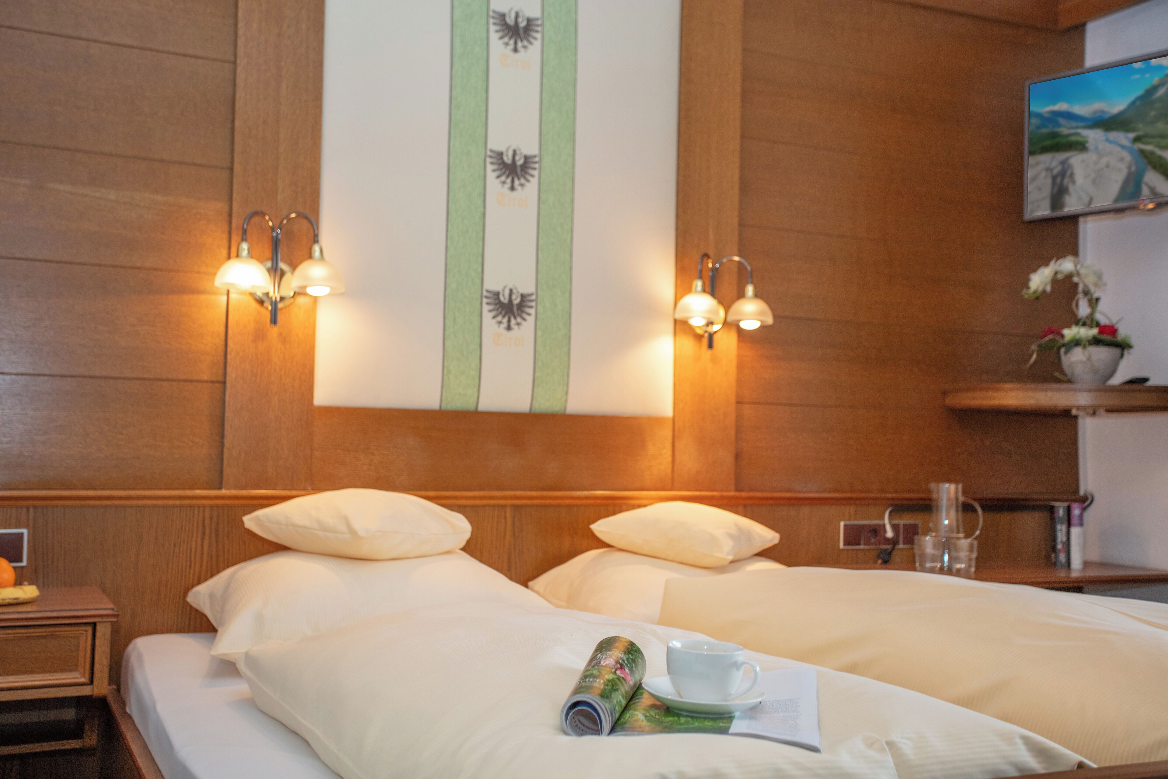 A hotel room with two beds, a painting on the wall, and a television.