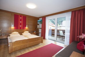 Ein modernes Hotelzimmer mit einem hölzernen Bett, einer roten Akzentwand und Blick auf einen Balkon mit Gartenmöbeln.