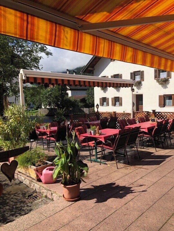 Eine Außenpatio mit Tischen und Stühlen, umgeben von Pflanzkübeln und einem Gebäude mit Fenstern.