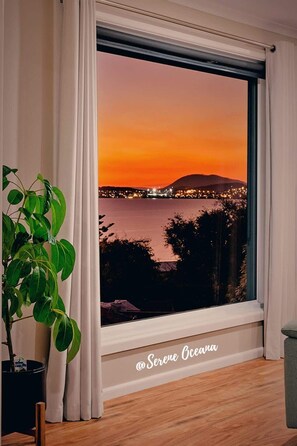 Et værelse med stort vindue, der udover en solnedgangsudsigt over by og vand.