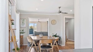A dining area with a wooden table and chairs, a ceiling fan, and a view of the outdoors.