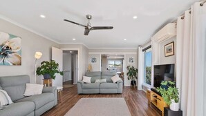 A modern living room with a grey sofa, a grey couch, a flat-screen TV, and a ceiling fan.