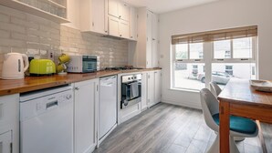 A modern kitchen with white cabinetry, a built-in oven, a dishwasher, and a dining area with a wooden table and chairs. - One Bedroom Apartment to Sleep 2 in the Heart of Kenmare Town (Kenmare)