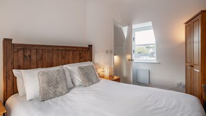A bedroom with a wooden headboard, a bed with white linens, a nightstand with a lamp, and a view of the outside through a window. - One Bedroom Apartment to Sleep 2 in the Heart of Kenmare Town (Kenmare)