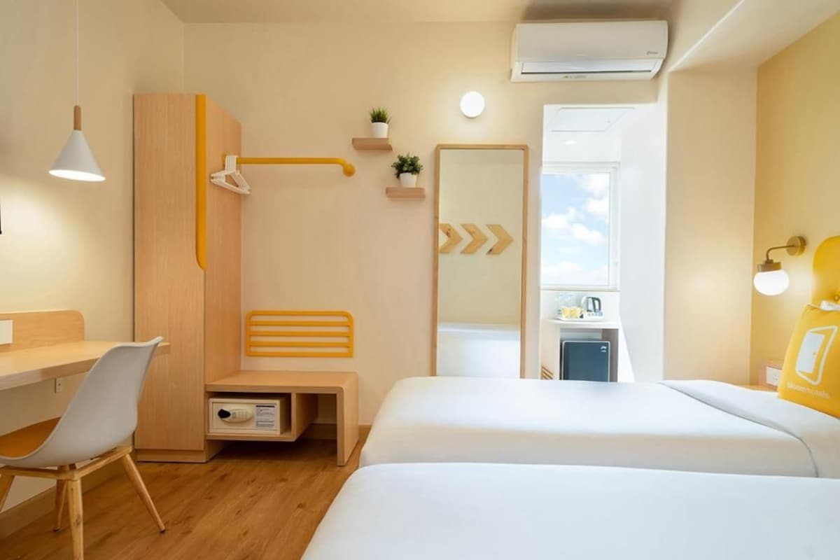 A hotel room with a desk, two beds, a shower, a mirror, and a small kitchenette.