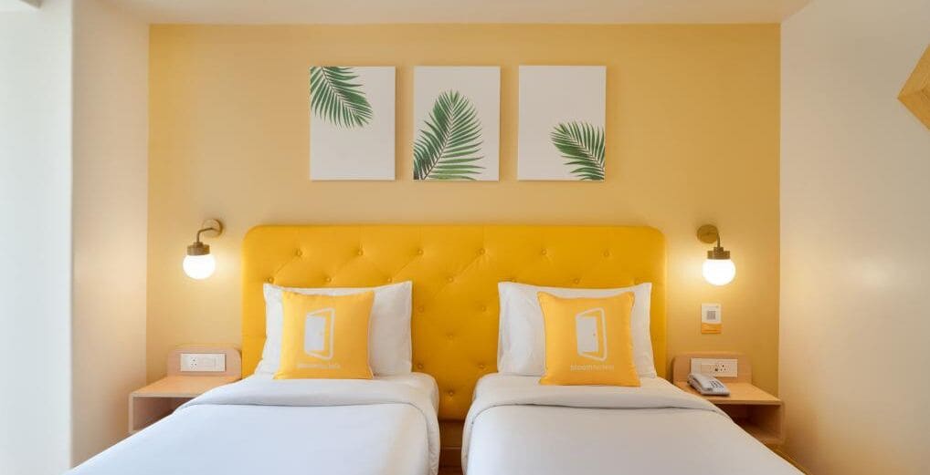 A double bed with yellow headboard and pillows, two bedside tables with lamps, and three wall-mounted leaf art pieces.