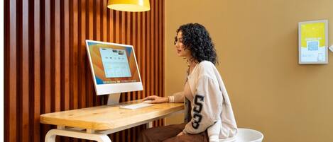 Una persona sentada en un escritorio de madera con una computadora, una lámpara colgante amarilla y un código QR en la pared.
