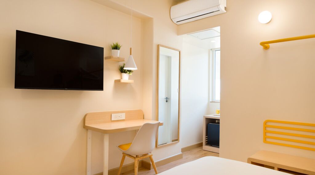 A modern hotel room with a flat-screen TV, a desk, a chair, a bed, and a bathroom visible through an open door.