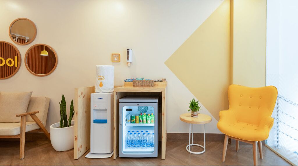 Une chambre d’hôtel de taille réduite, comprenant un canapé, une petite table avec une plante, un mini-réfrigérateur rempli de boissons et un réfrigérateur compact.