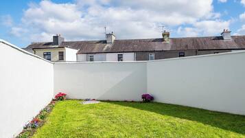 A small, enclosed garden area with a grassy lawn and flower beds, surrounded by a white wall.