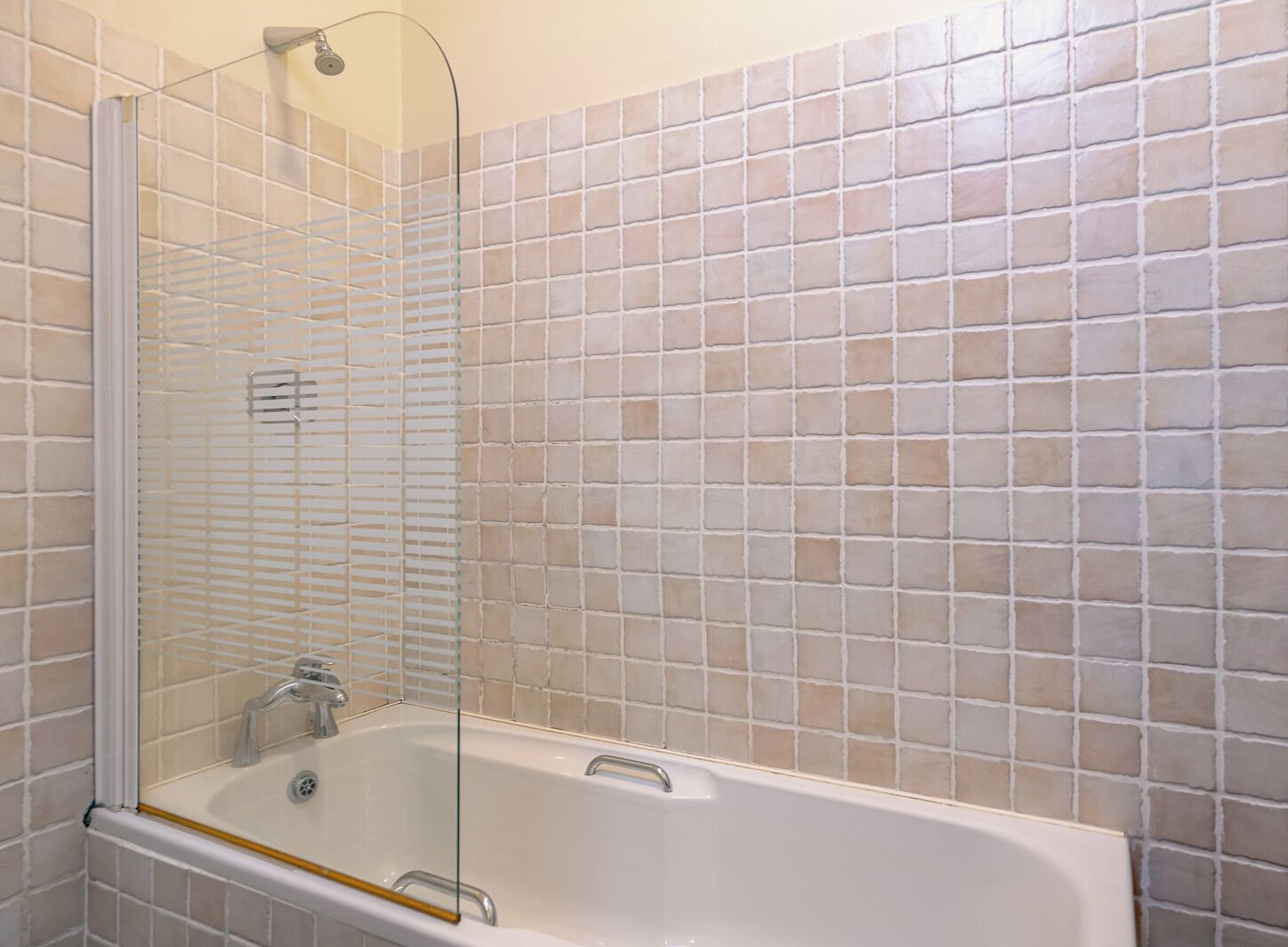 A bathroom with a bathtub, a glass shower enclosure, and beige tiled walls.