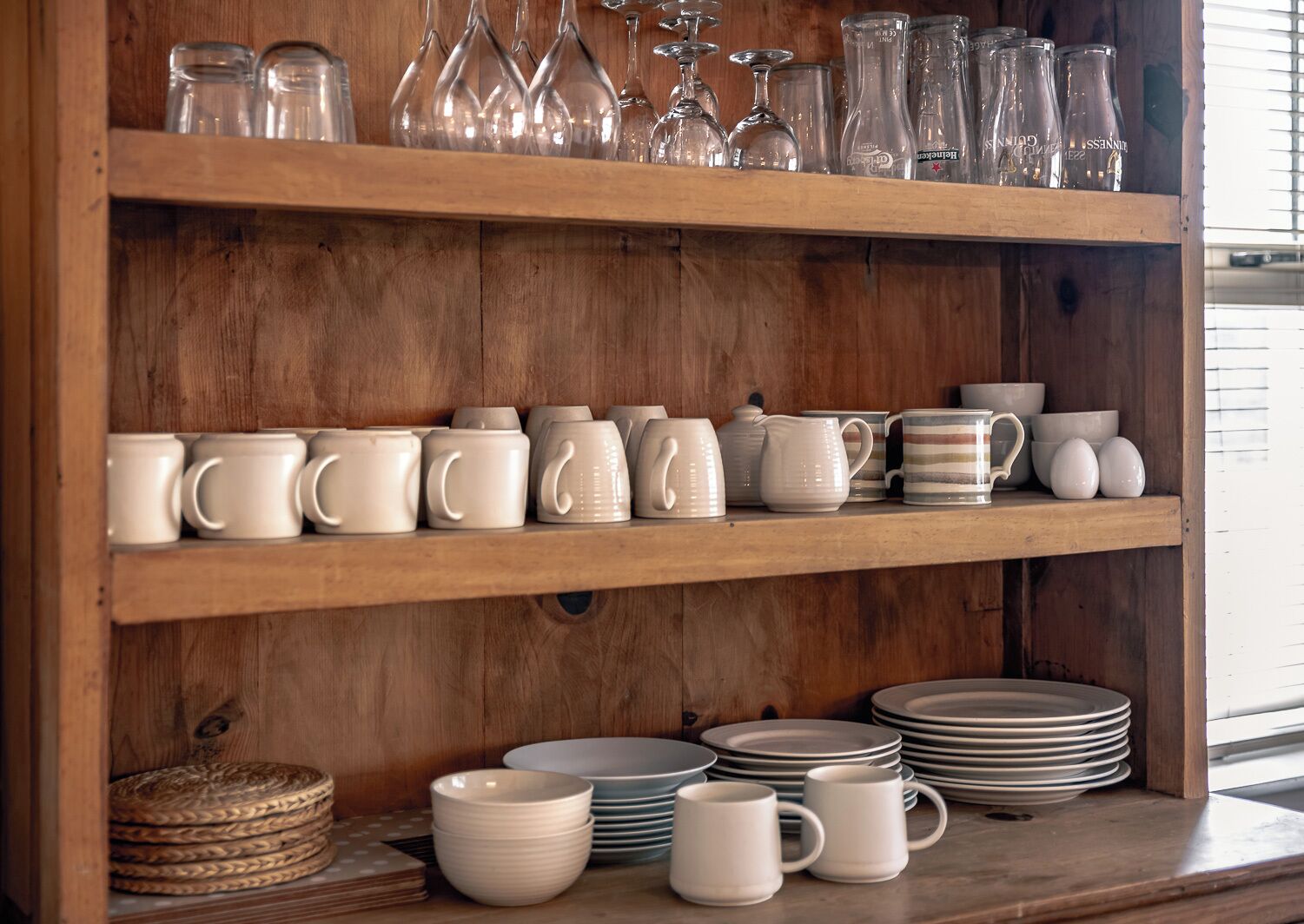 A wooden shelf unit with various glassware, ceramic mugs, and plates.