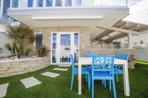 Un patio con una mesa blanca y sillas azules, rodeado por un muro de piedra y plantas de palma.