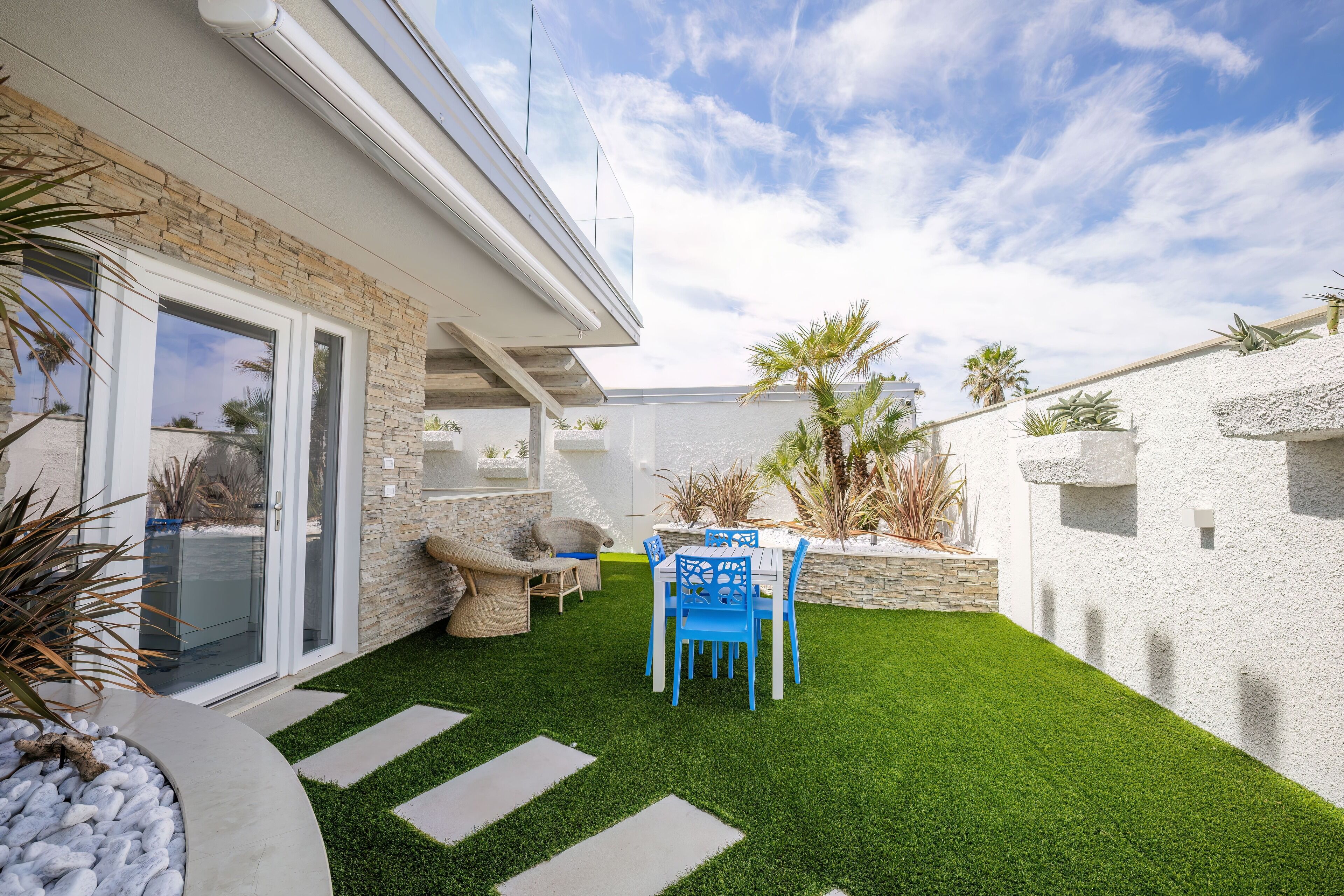 Une terrasse avec un ensemble de mobilier de jardin, un mur en pierre et un bâtiment blanc doté d’une porte en verre.