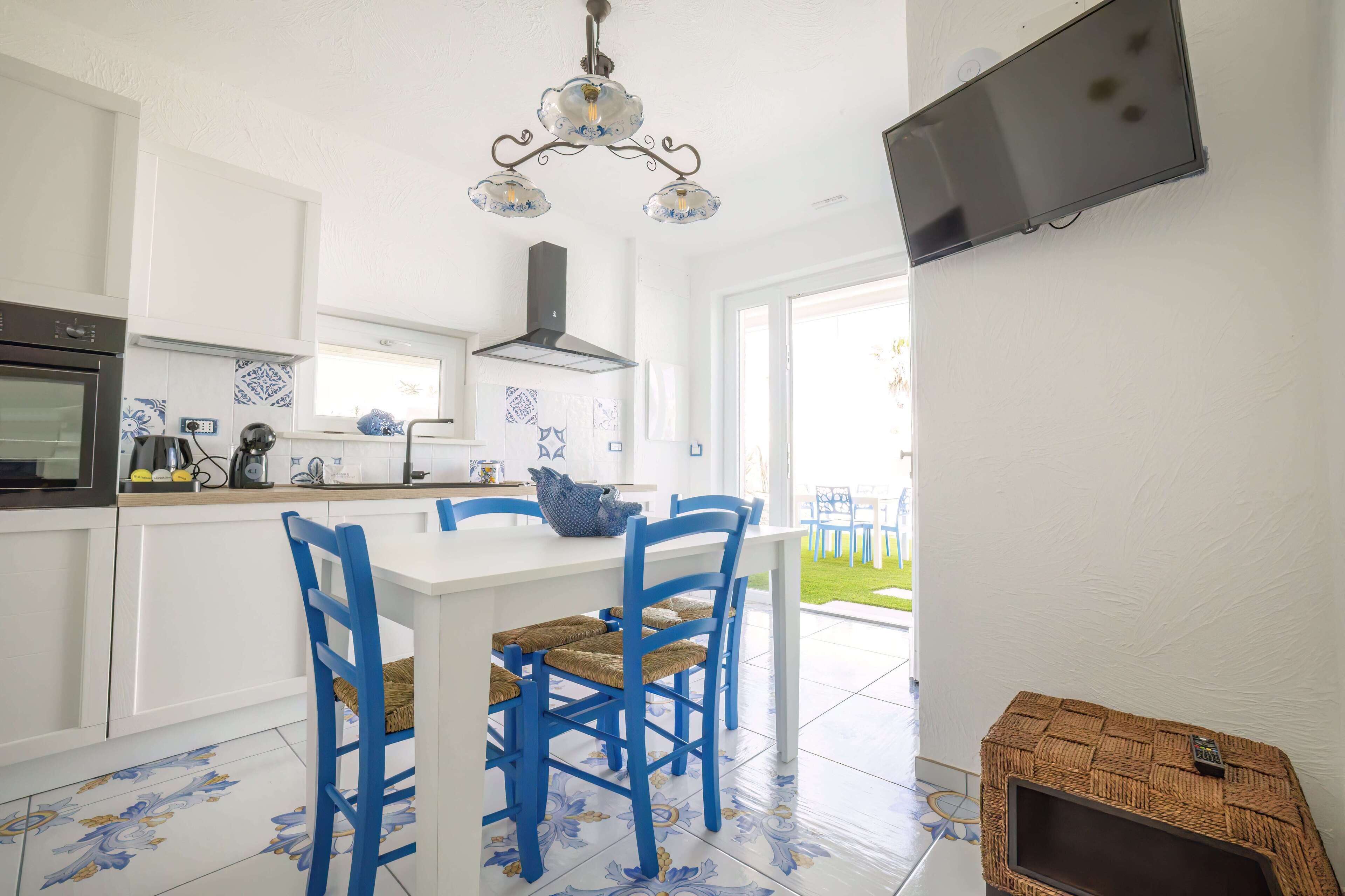 Een moderne keuken met witte kasten, een wit eiland, blauwe stoelen en een decoratieve plafondlamp.