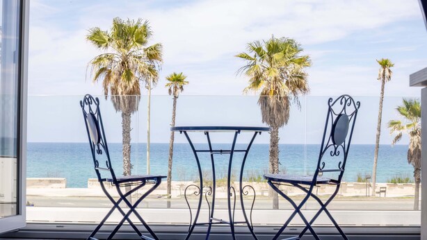 A balcony with two chairs and a table, overlooking the sea and palm trees. - Etoiles Guest House (Gioia Tauro)
